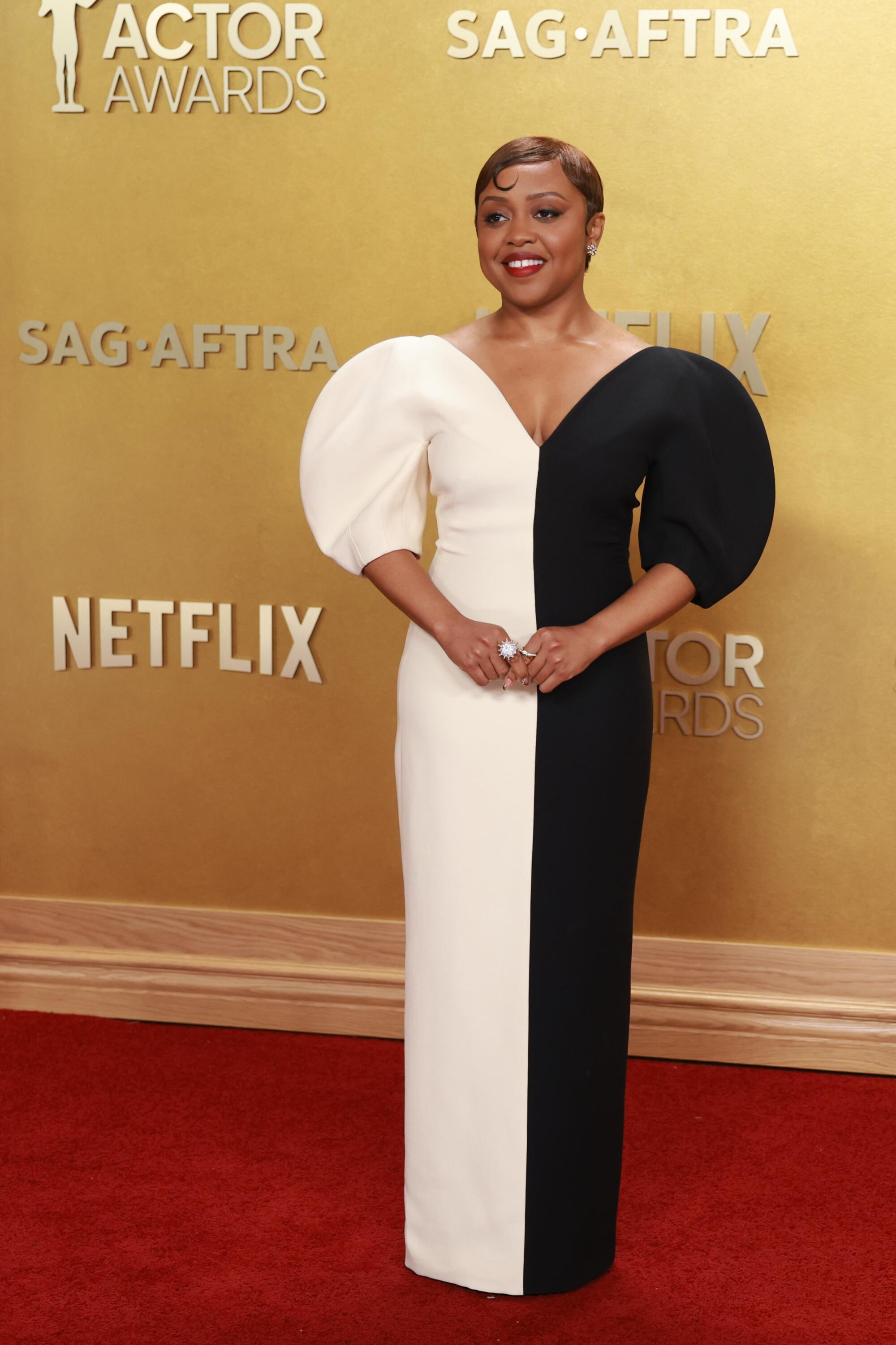 Quinta Brunson, wearing a half-white-half-black dress, poses on the red carpet. 