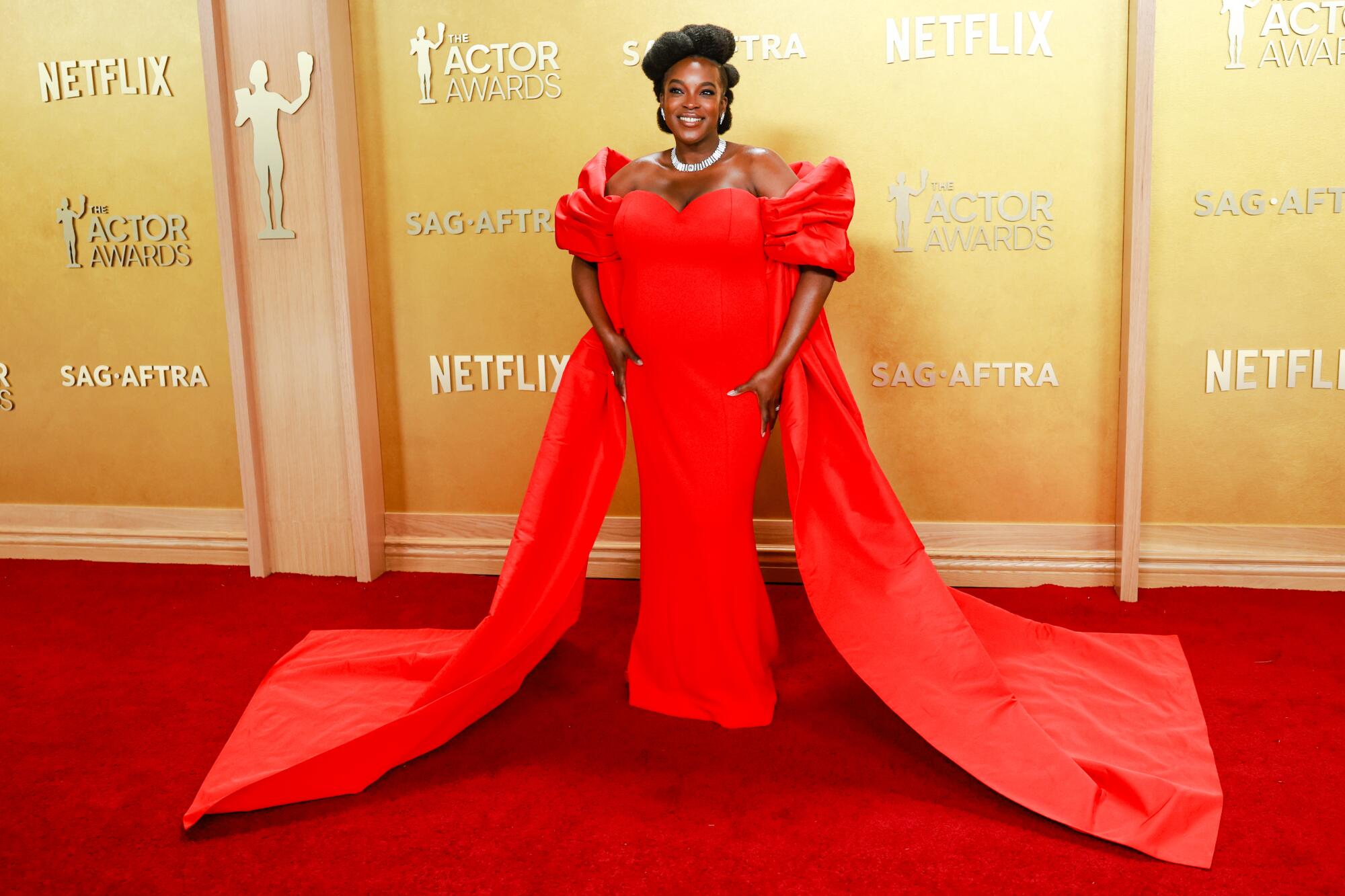 Wunmi Mosaku, wearing a red cape gown, poses on the red carpet. 