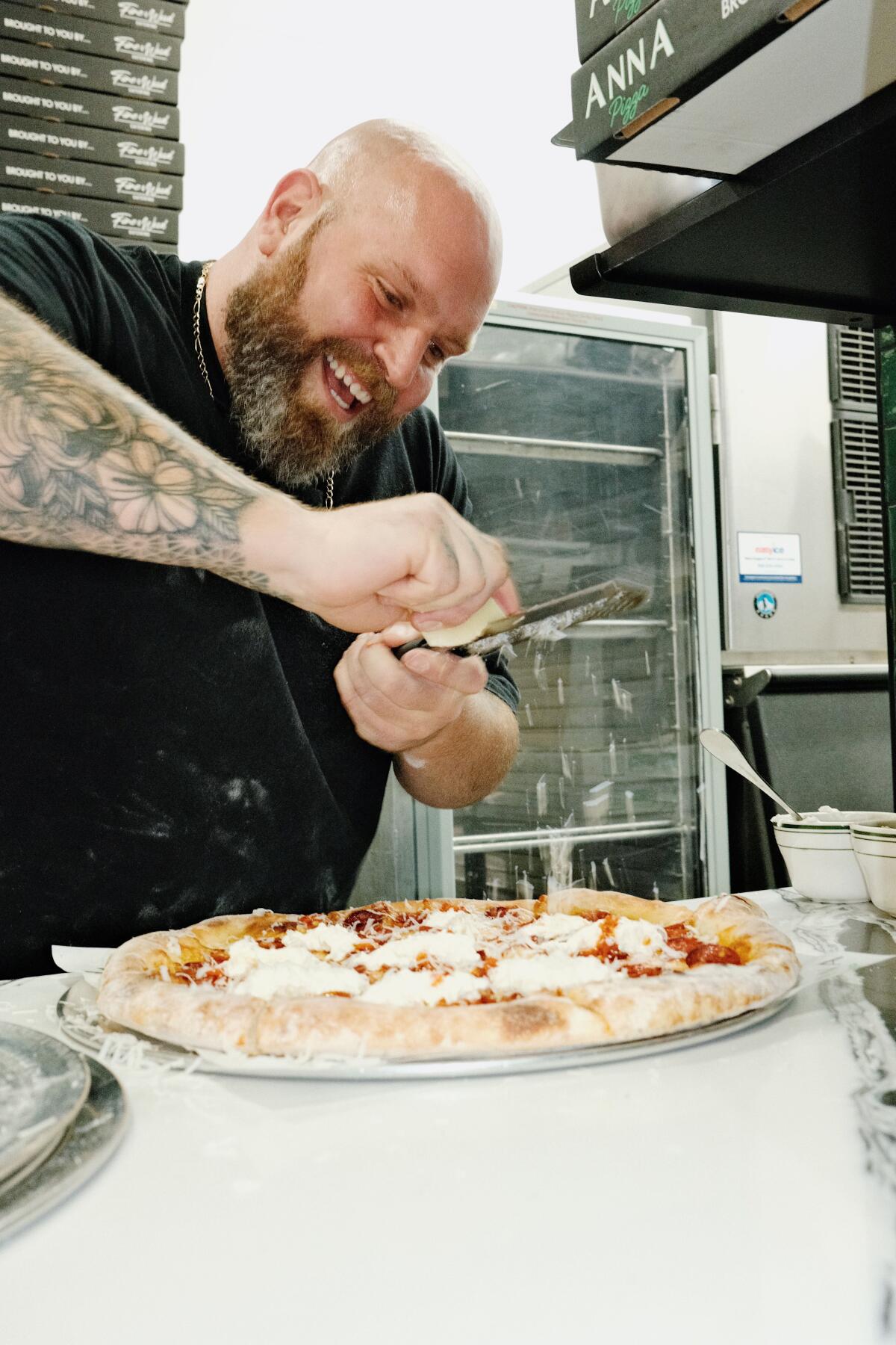 Anna Pizza chef-owner Thomas DeSantis grate cheese onto a pizza in a kitchen