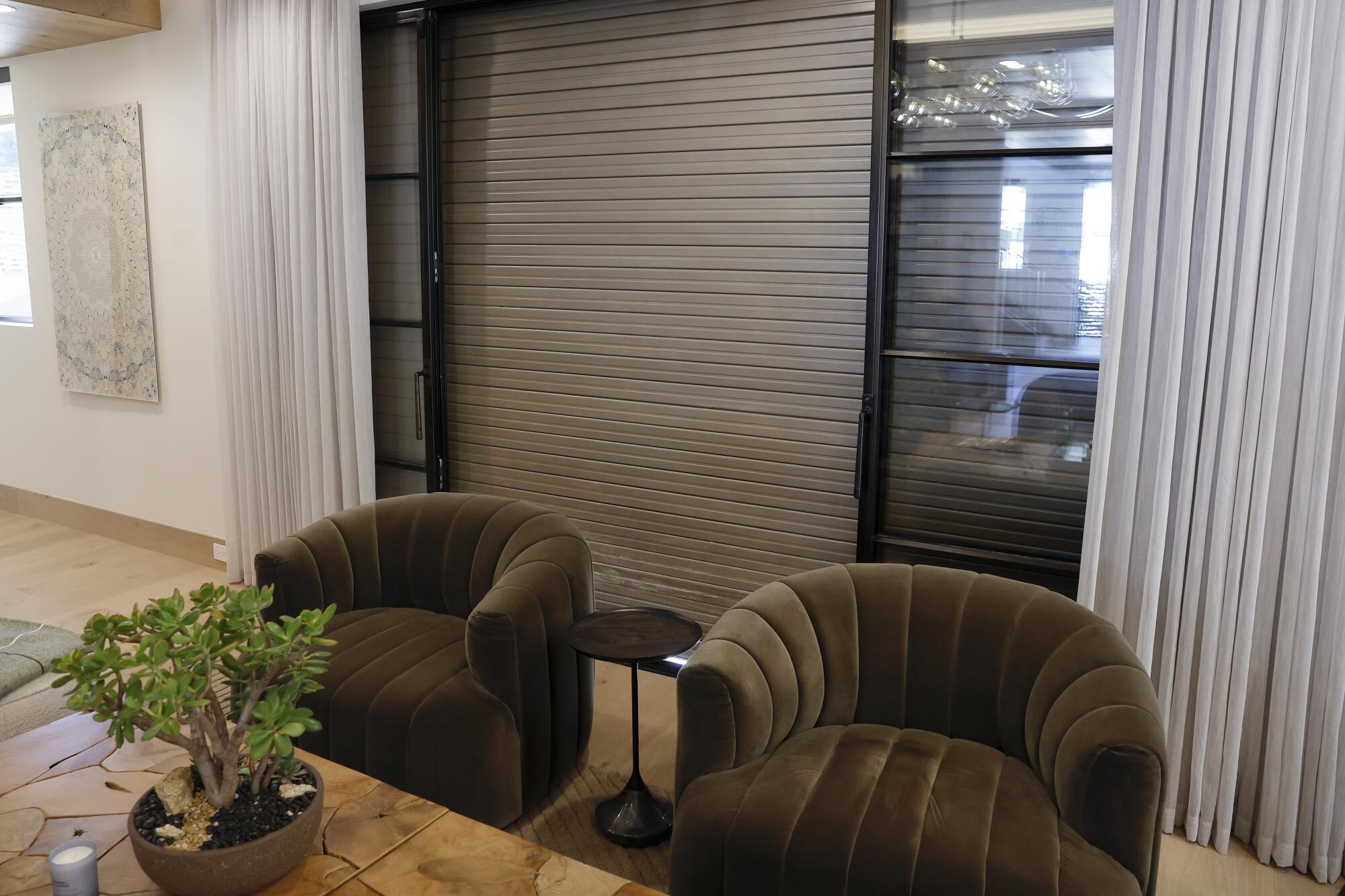 A living room inside a fire-resistant house, with metal heat shields drawn over the windows. 