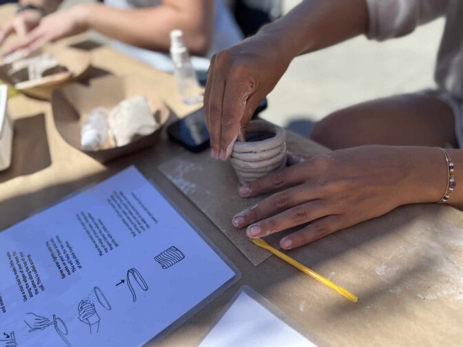 Two hands work a clay pot on a table.