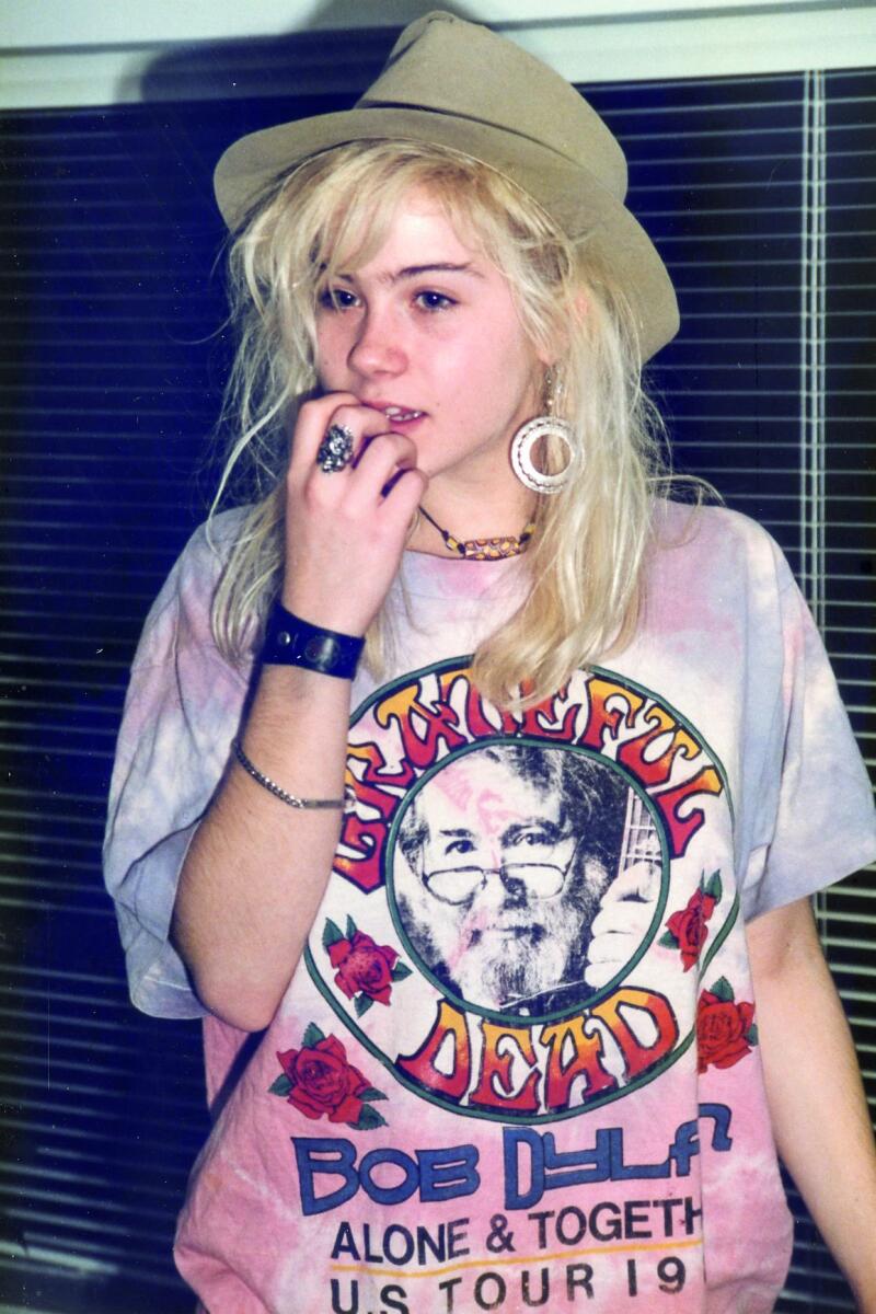 A young Christina Applegate wearing an oversized graphic T-shirt and a hat.