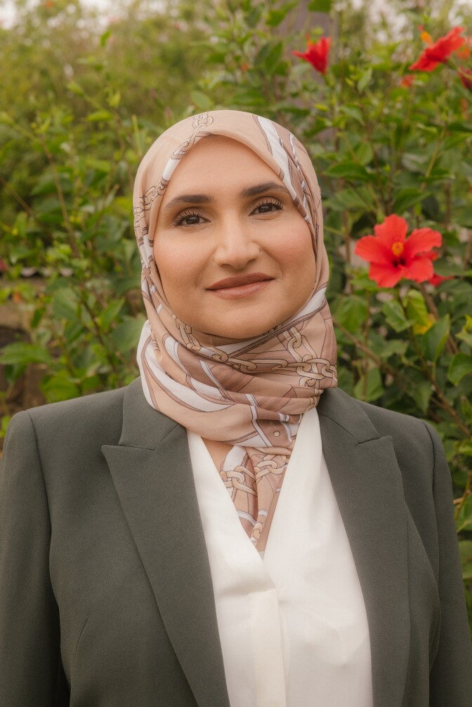 A woman with medium skin tone and a head covering poses for a portrait. 