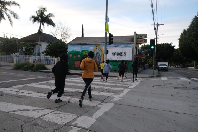 A group of people run across a street towards a market and small shops.