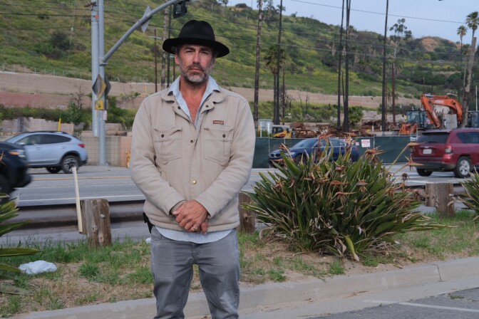  Rashi Kaslow, a man with medium skin tone, stands in a beach parking lot across from the Palisades Bowl mobile home park, where residents' burned cars still haven't been removed.