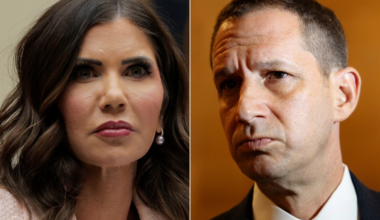 A woman with long dark hair and pearl earrings looks attentive, while a man with short dark hair and a serious expression wears a suit and tie.