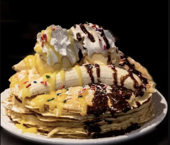 A plate of pancakes, loaded with chocolate syrup, bananas, whipped cream, lemon curd and chocolate syrup