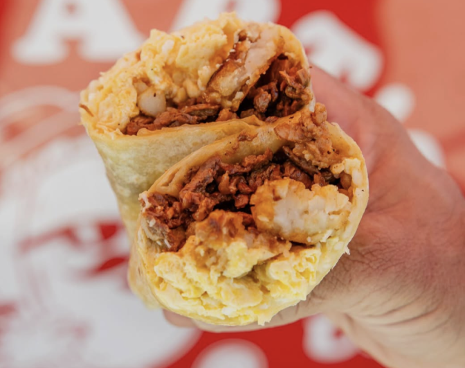 Two halves of a breakfast burrito, containing brown juicy meat, eggs, cheese and rice