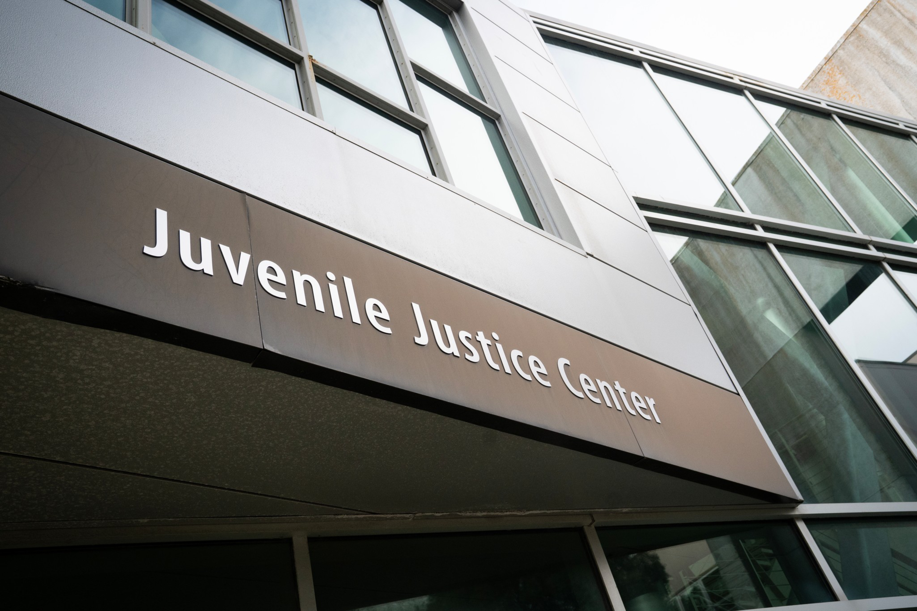 A modern building facade with large glass windows and a sign reading “Juvenile Justice Center” in white letters on a brown panel.