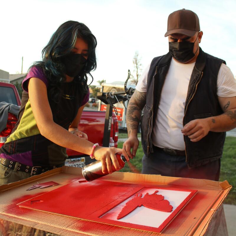 Muñoz supervises as his stepdaughter Venus, left, spraypaints his design into the signs. 