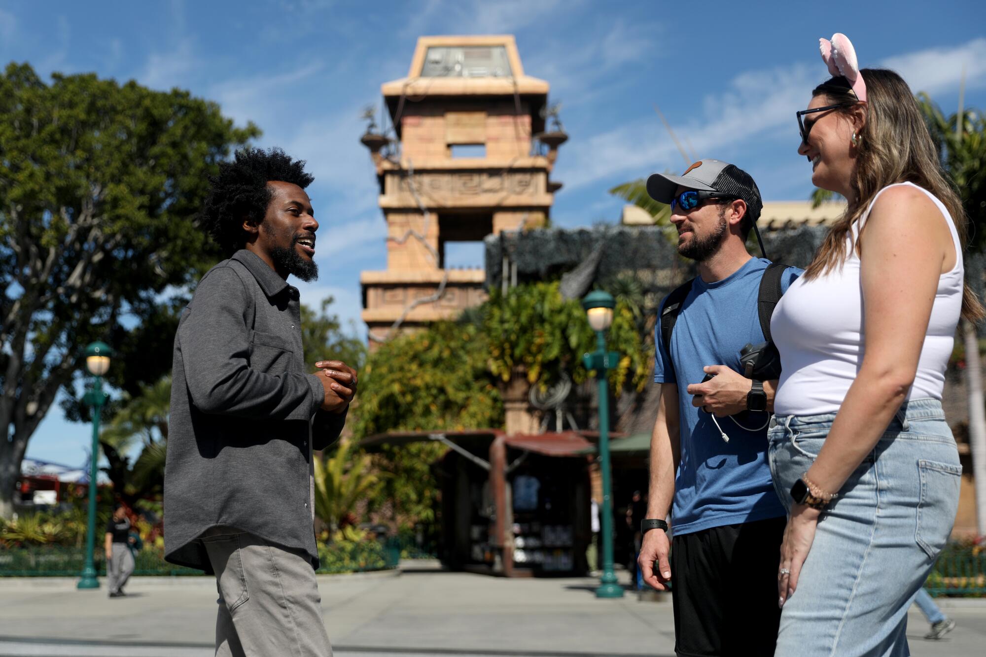 Three people chat in front of an earth-toned tower.