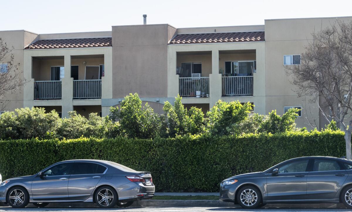 Two cars on a street in front of hedges and a two-story building.