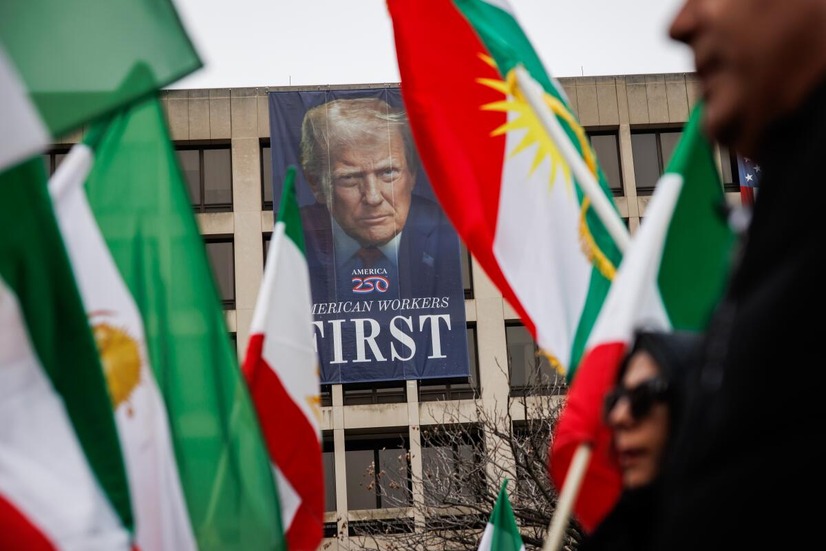 Demonstrators march past a banner depicting President Trump.