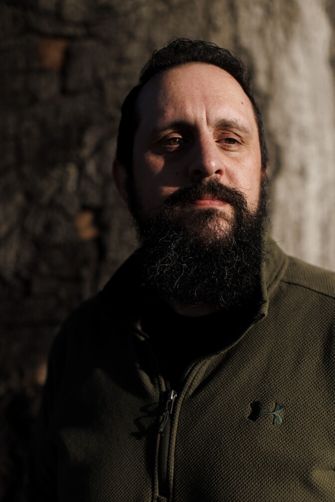 A man with dark hair and a dark beard looks slightly off camera.