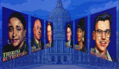 A man with curly dark hair and light facial hair wears a white shirt featuring large blue fish illustrations.