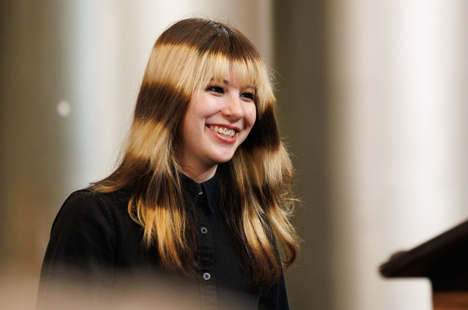 A crowd of young people, many holding phones, with one person holding a colorful sign that says “Congrats Ilyssa Liu, You’re Cooler Than Ice.”