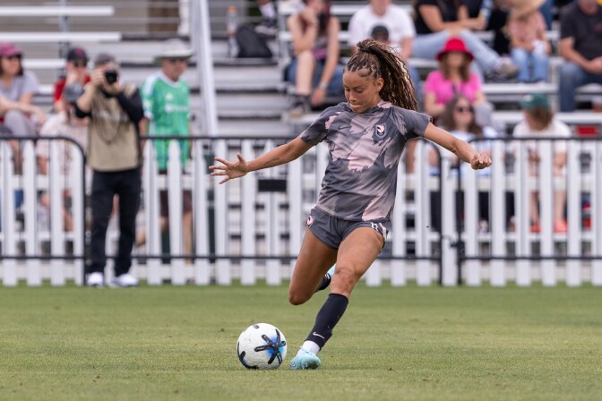 A medium-skin-toned Black woman prepares to kick a soccer ball.