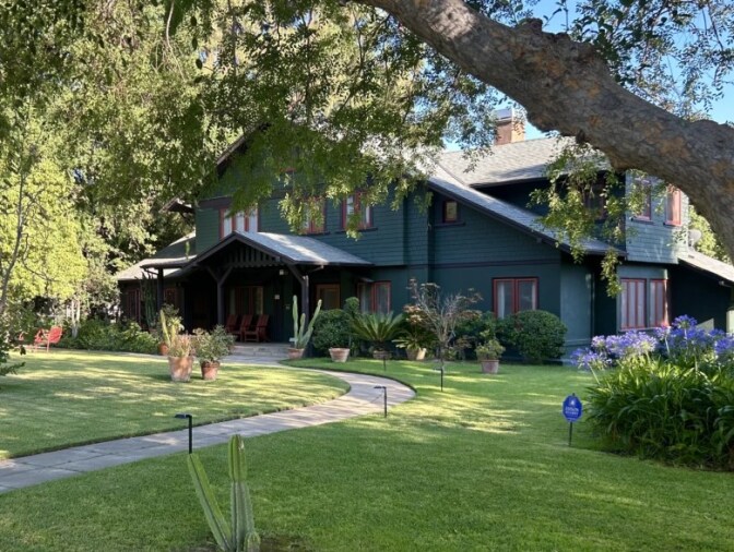 A green crafstman style home with a large green lawn and a wnding concrete path