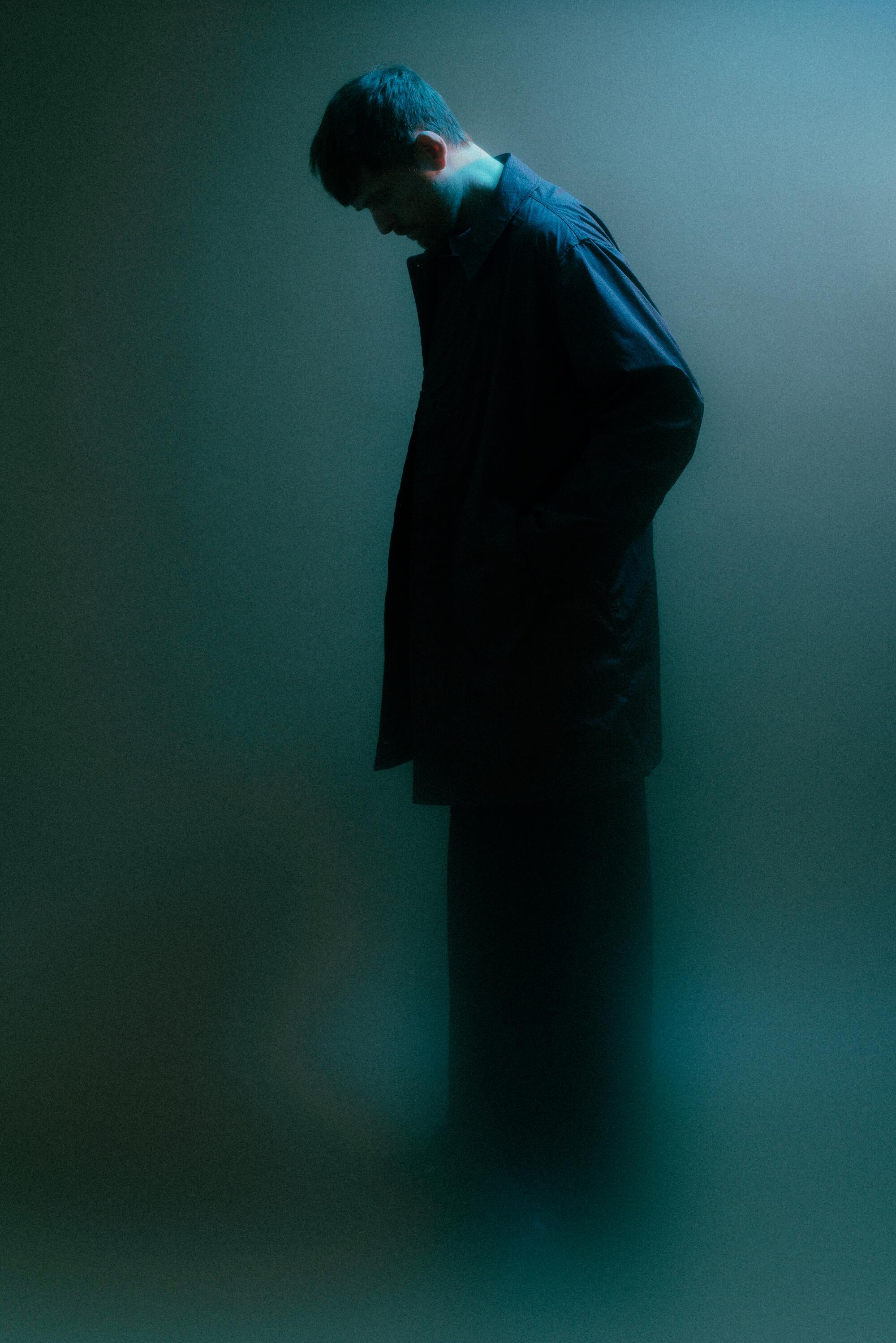 James Blake poses standing upright with a long coat