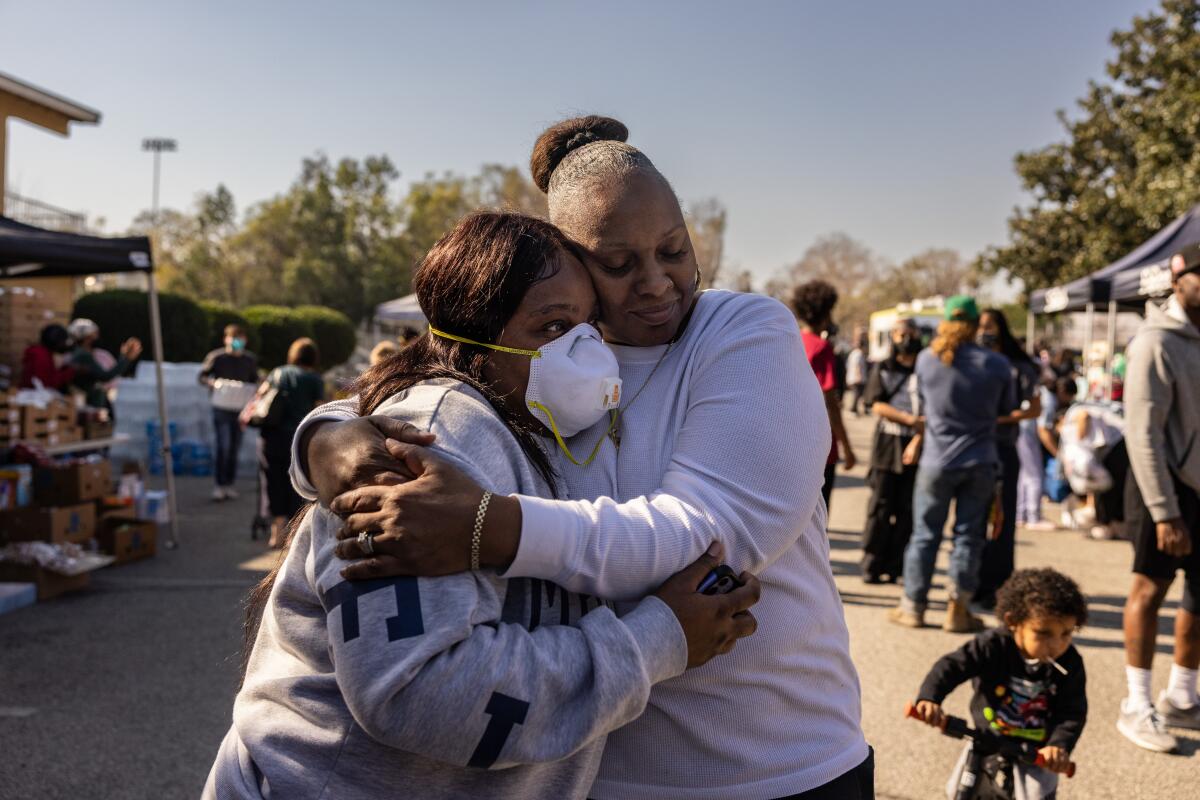 Two people, one wearing a face mask, embrace.