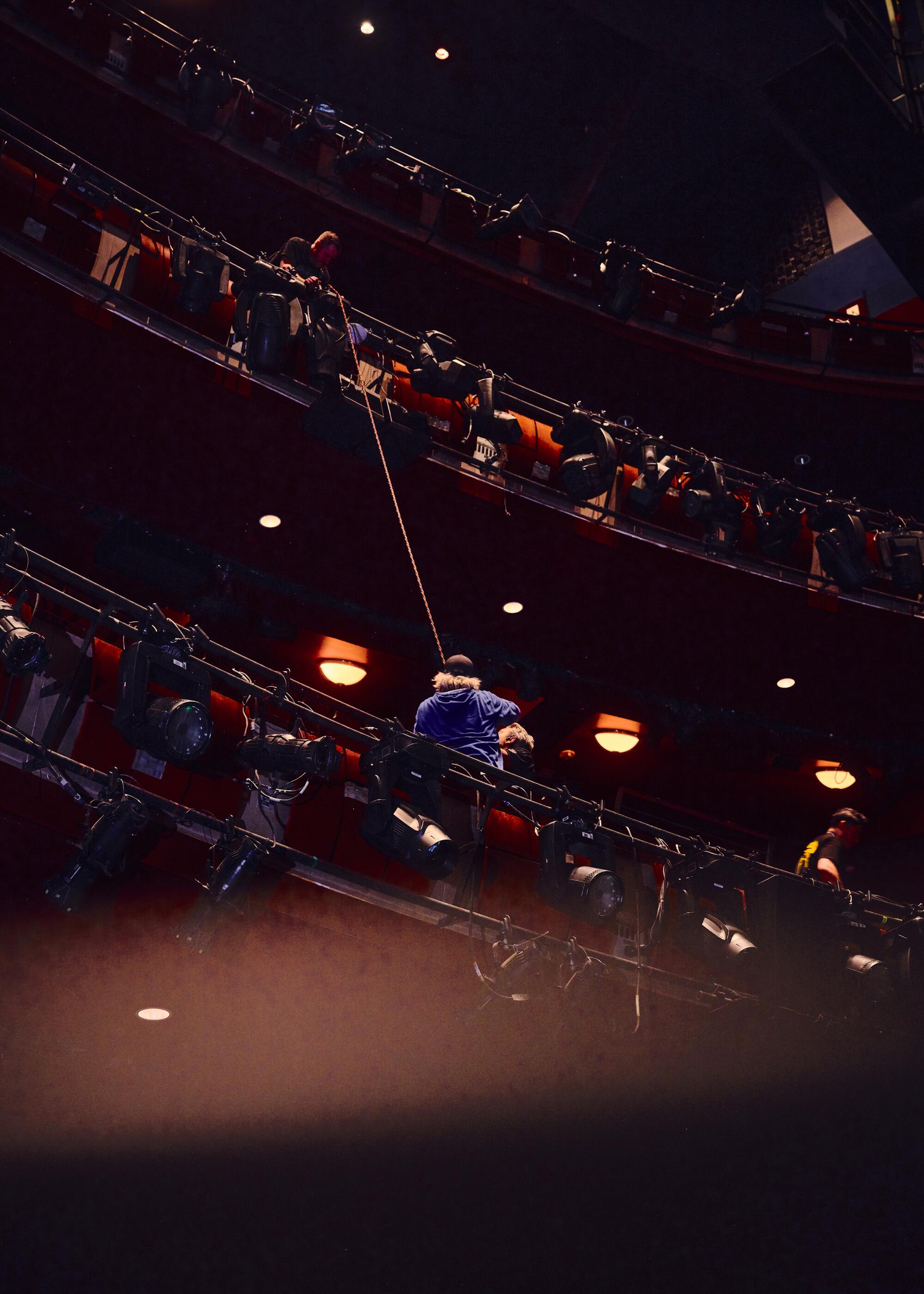 An electrician rigs lights on the balcony of the theater.