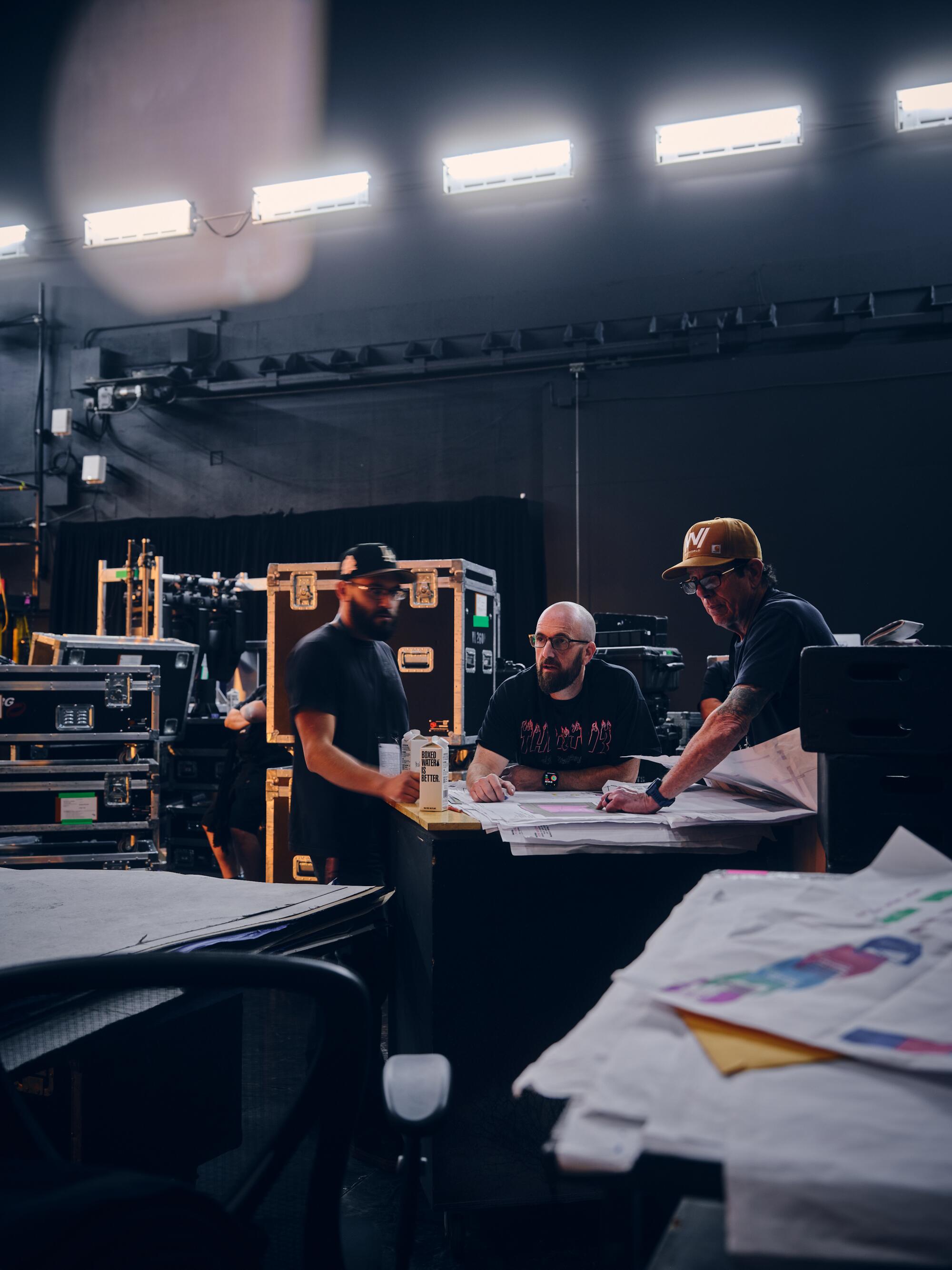 A team of three men huddle over production plans backstage. 
