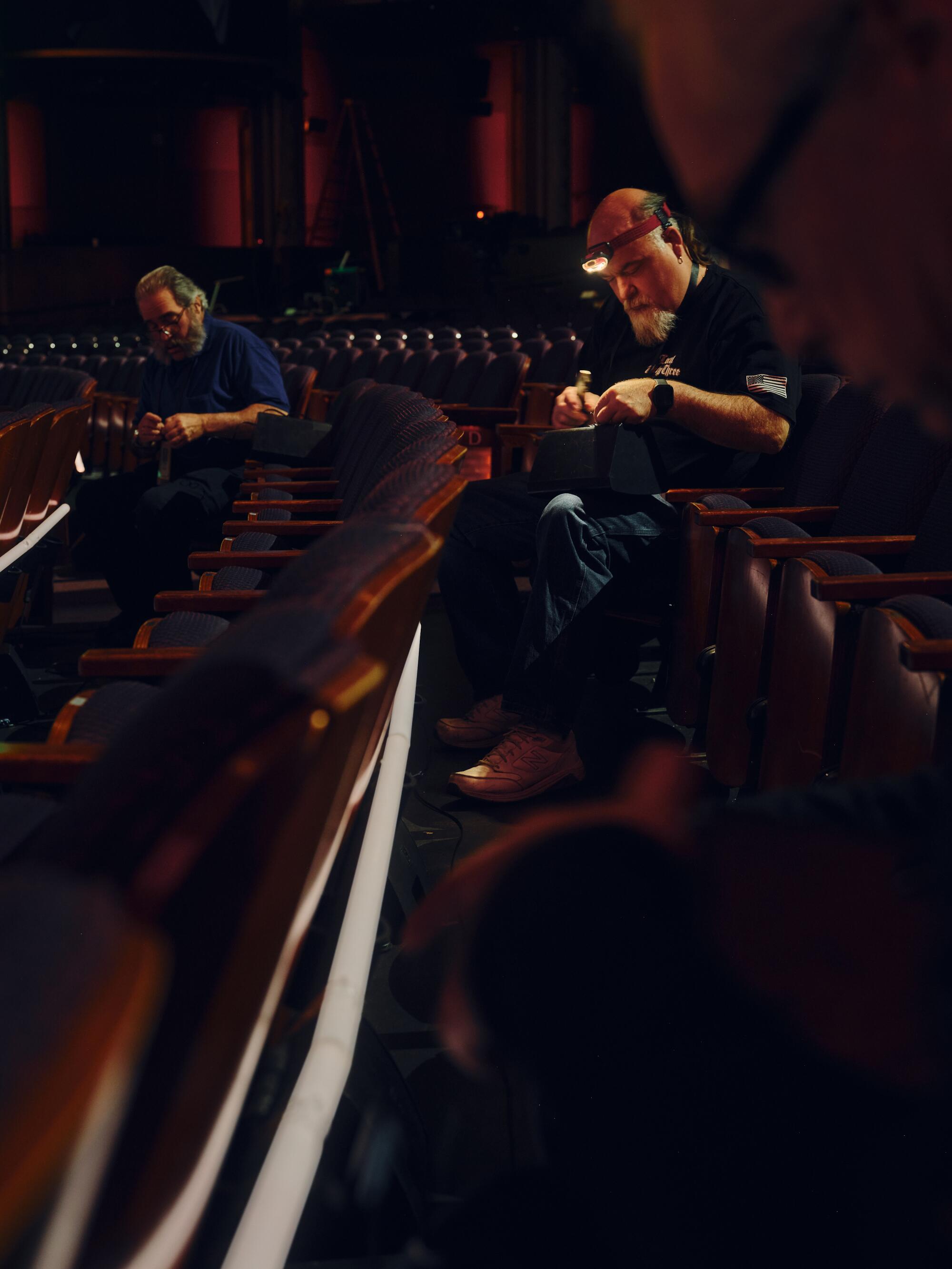 Two electricians place lighting strips along the orchestra seats of the theater.
