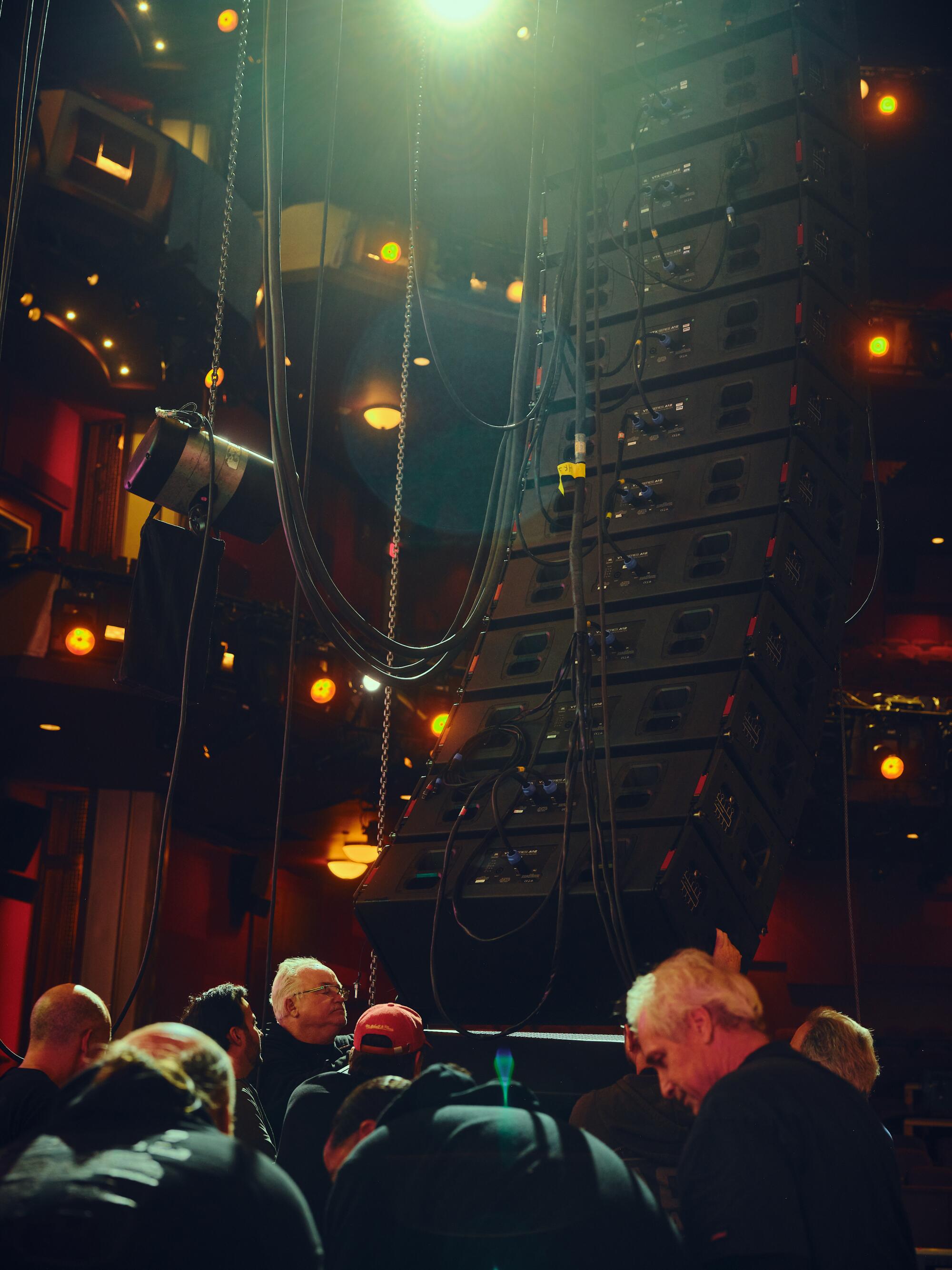 A crew hoists a large speaker up. 