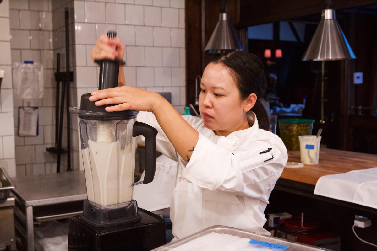 A woman works at a blender in a professional kitchen