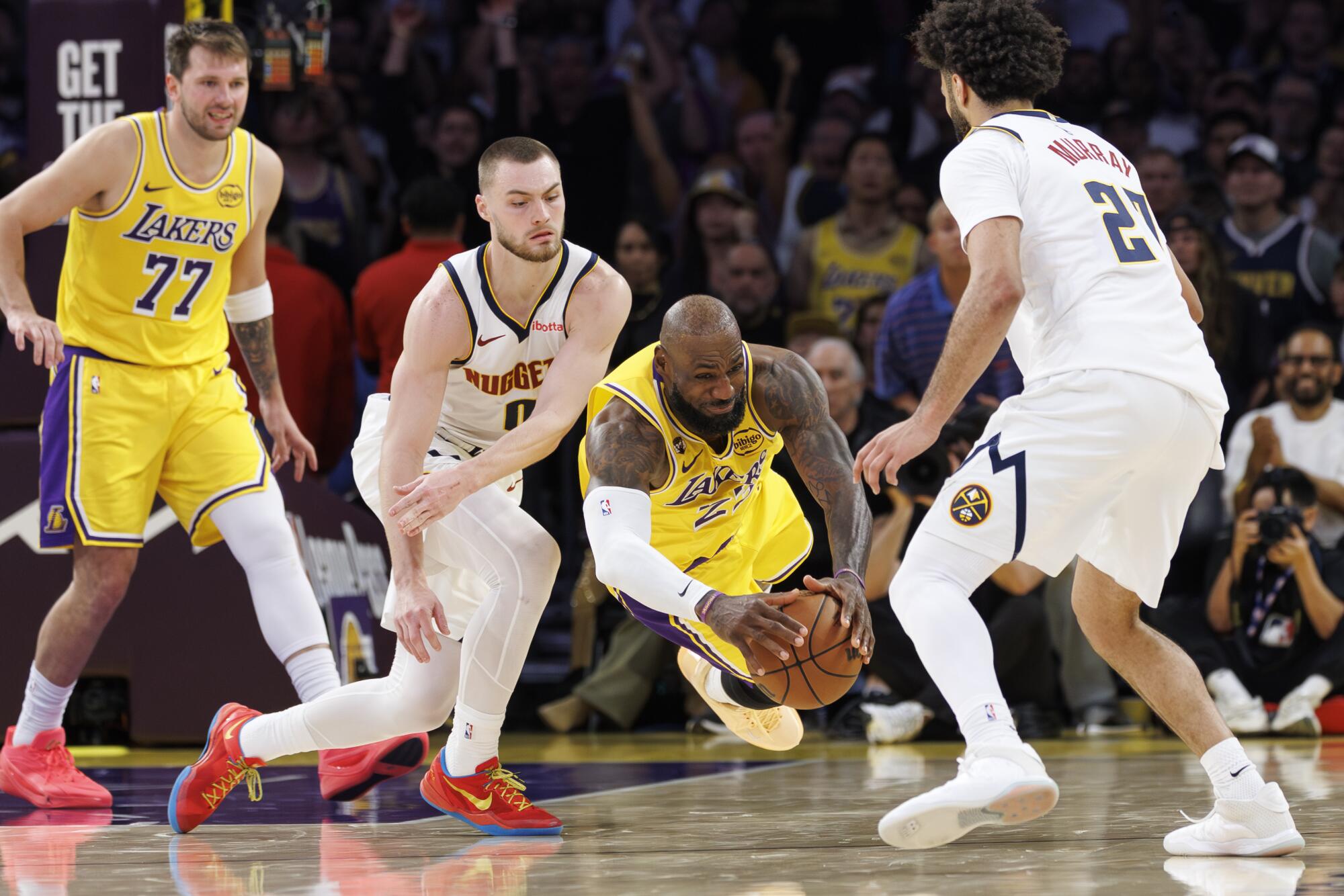 Lakers star LeBron James dives for the ball between Denver Nuggets guards Christian Braun (0) and Jamal Murray.