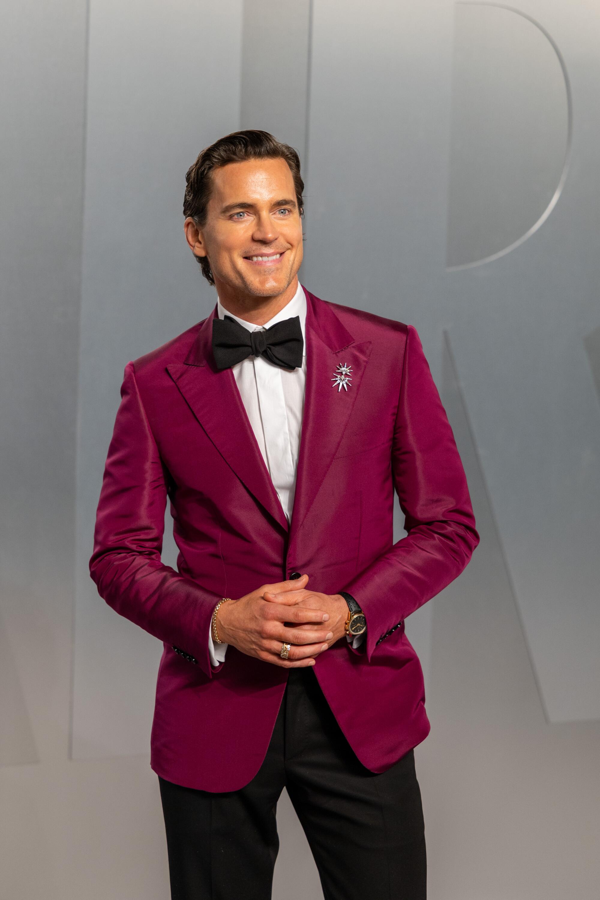 Matt Bomer, wearing a fuchsia blazer, poses on the red carpet. 