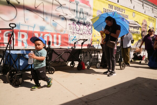 People cover themselves from the heat with umbrellas while waiting at a food distribution site Wednesday, March 11, 2026, in Los Angeles. (AP Photo/Damian Dovarganes)