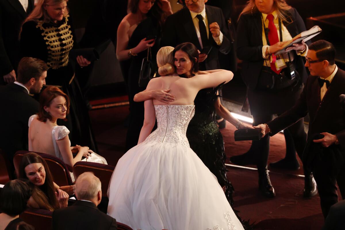 Two women in gowns hug.
