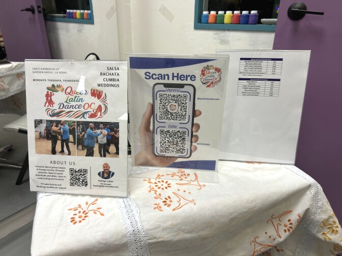 A small square table covered in a qhite tablecloth. On top are three flyers.