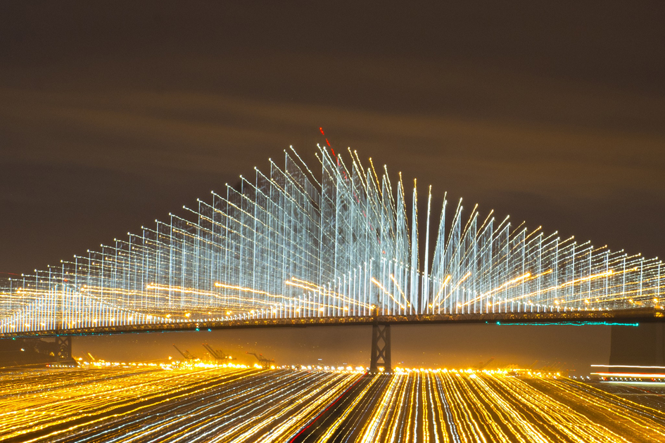 A light show illuminating cables on a suspension bridge shine at night.