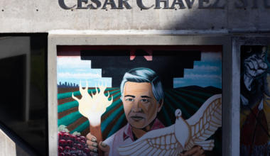 A mural of Cesar Chavez holding a flaming torch in one hand and a white dove in the other, with farmland and mountains in the background.