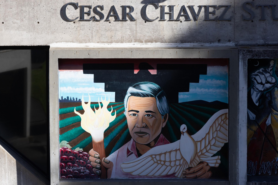 A mural of Cesar Chavez holding a flaming torch in one hand and a white dove in the other, with farmland and mountains in the background.