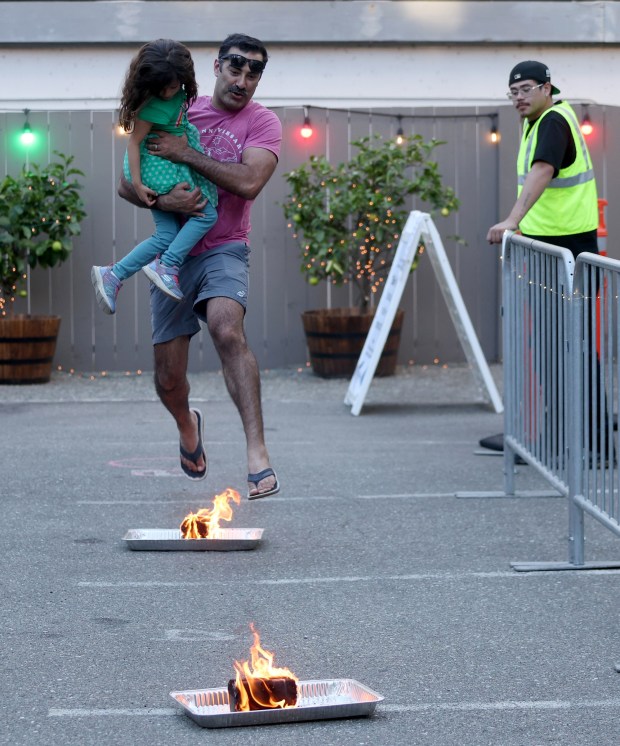 Shahad Asghar and his daughter Tara, 4, of Orinda, leap over fire logs during the Persian New Year Festival on Durant Avenue in Berkeley, Calif., on Tuesday, March 17, 2026. (Jane Tyska/Bay Area News Group)