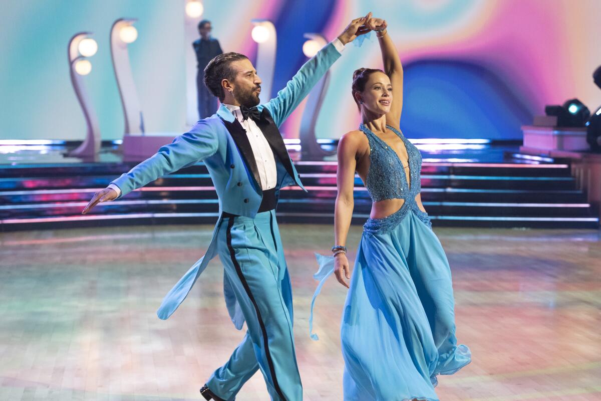 A man in a blue tuxedo and a woman a blue dress dance together.