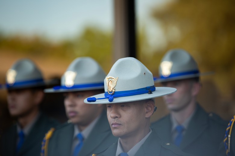 A close frame of a person wearing a CHP police uniform, with straight brimmed hat. In the background, more officers in the same uniform are out of focus, but visible.