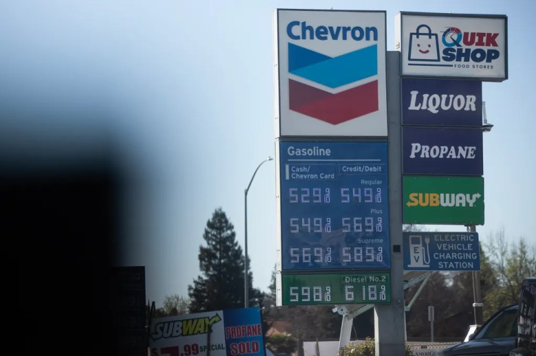 A Chevron gas station sign displays fuel prices for regular, plus, supreme, and diesel. Additional signs advertise a convenience store, liquor, propane, Subway, and an electric vehicle charging station.