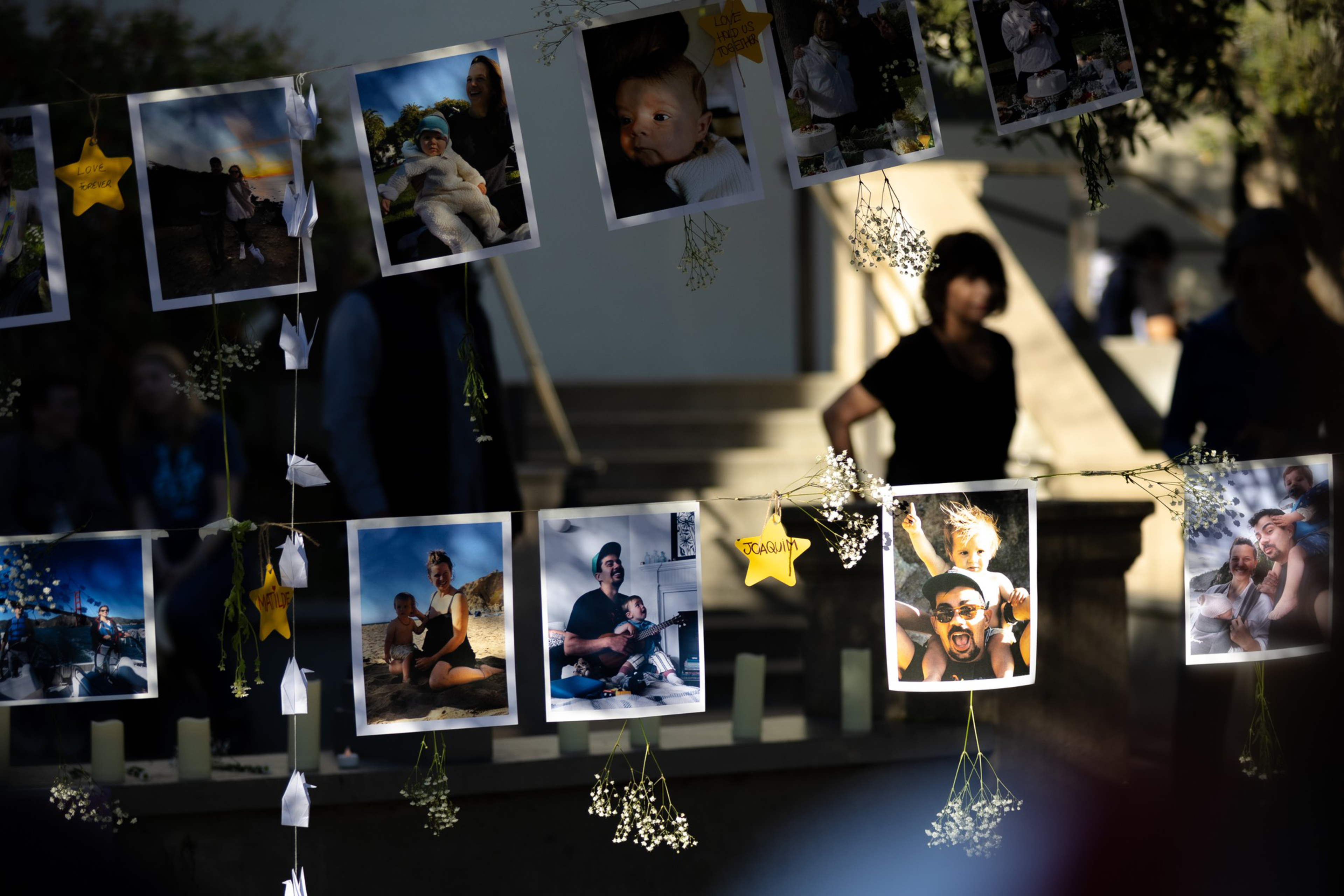 Photos of various people, including children and families, hang on strings with small white flowers and yellow star-shaped notes attached.