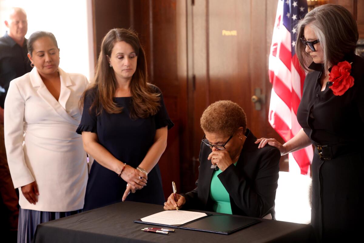 An emotional Mayor Karen Bass signs a proclamation with supporters flanking her