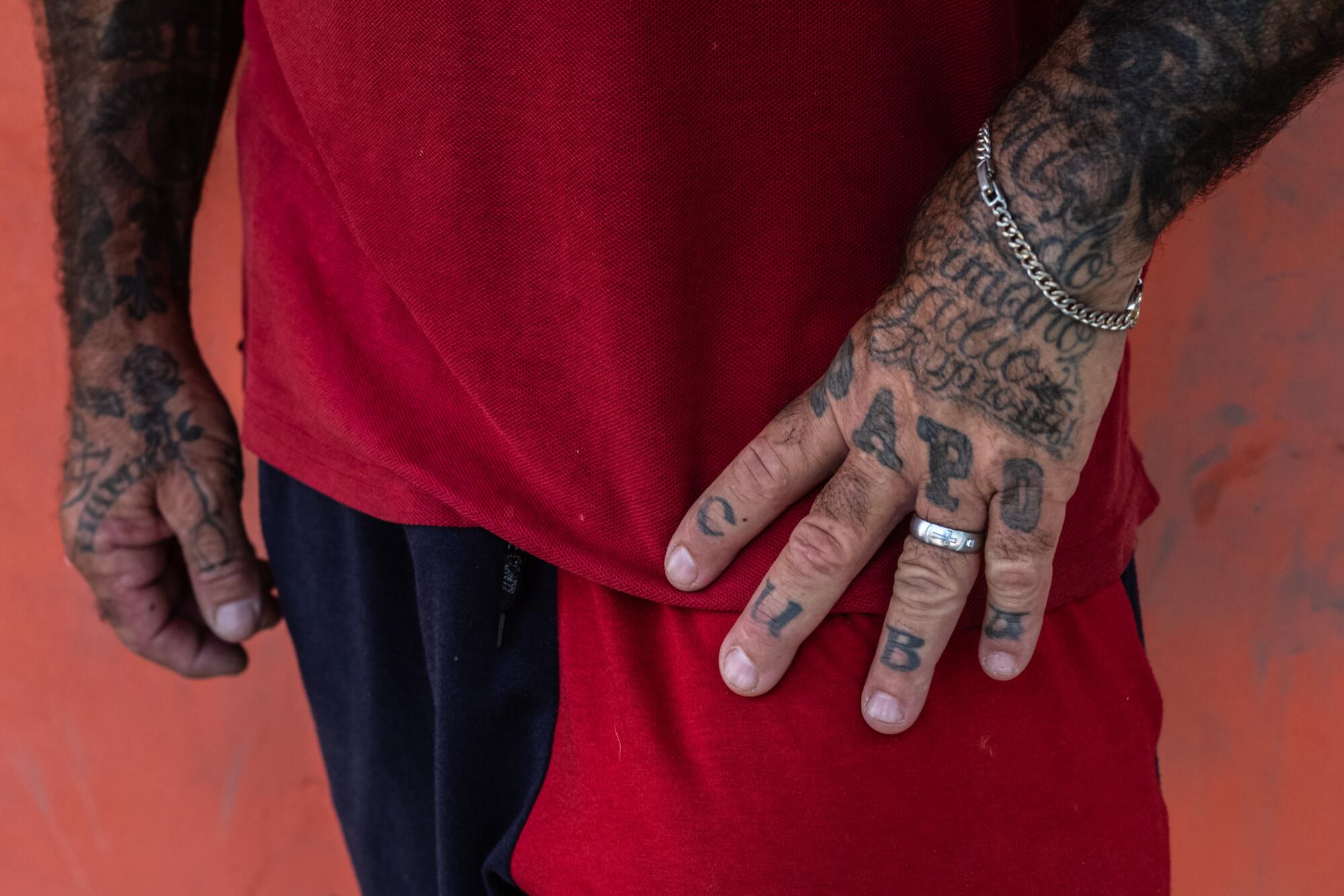 a deatil of a person in a red shirt with showing his tattooed hands