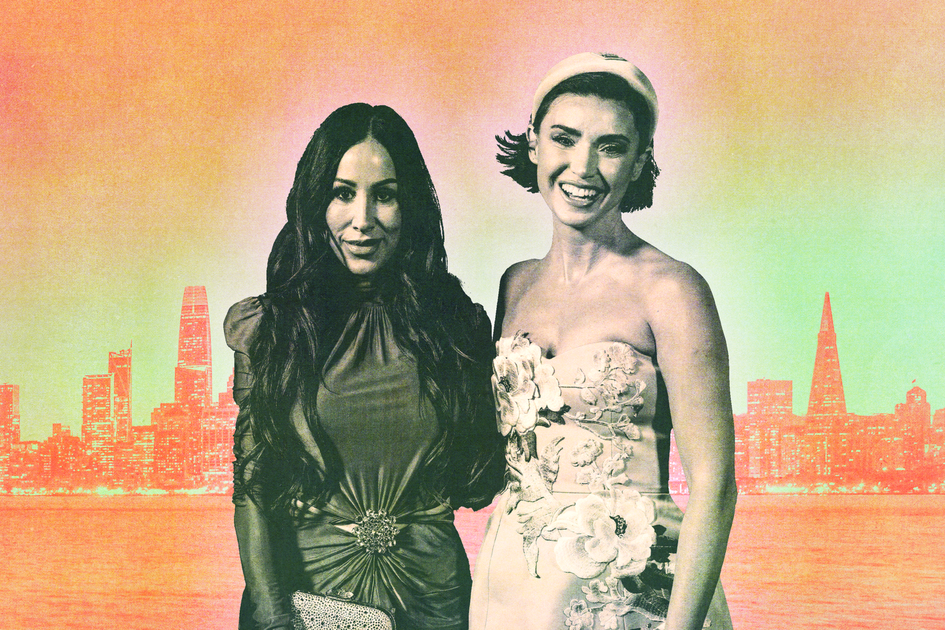 A woman with wavy, light brown hair wears tortoiseshell glasses, bright pink lipstick, a black blazer, and a black and white patterned high-neck top.