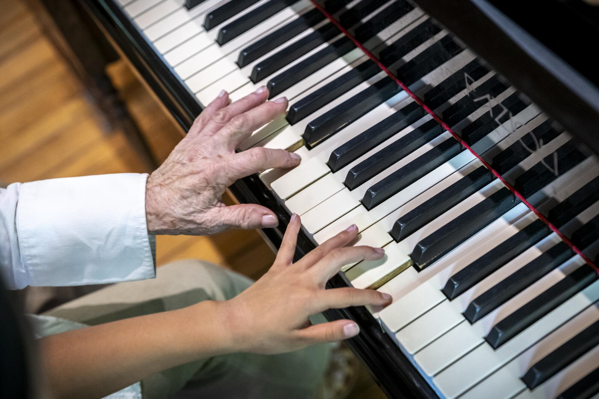 Two left hands next to each other play on a piano.