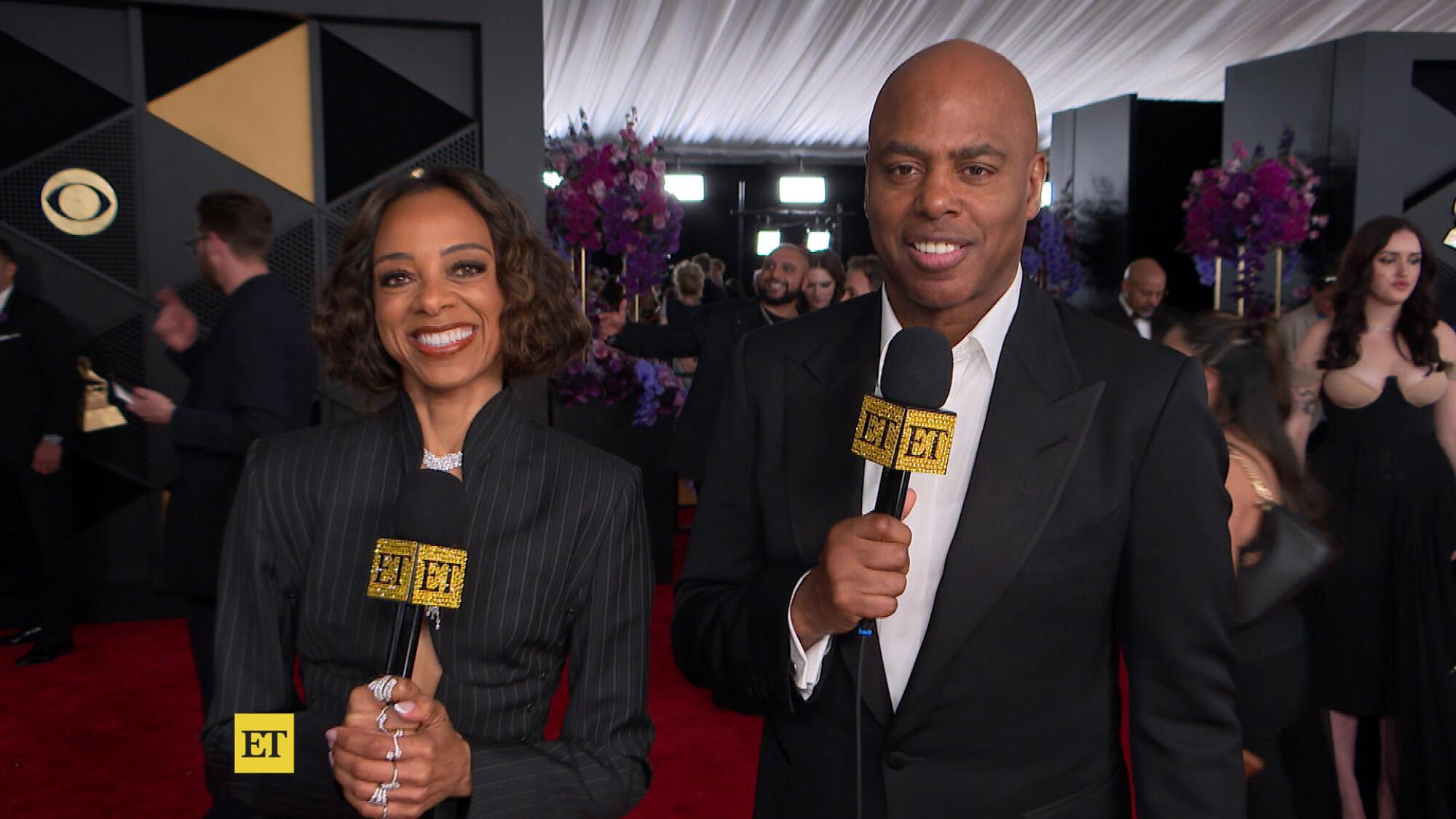 A woman and a man in black clothing holding microphones on a red carpet.