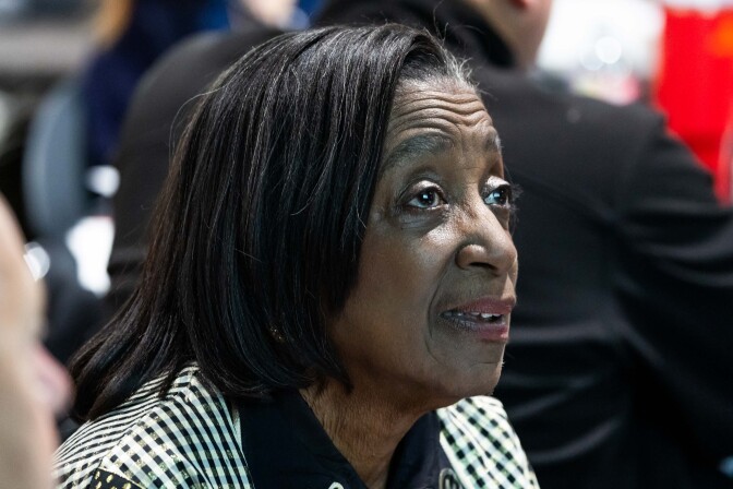 A woman with dark skin tone and short dark hair wearing a black and white coat. 