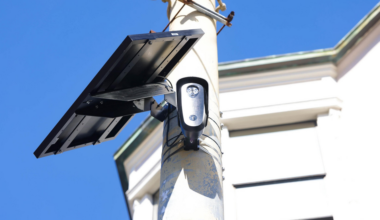 A woman in an orange shirt holds hands with a child wearing a brown hat as they sit on a metal bench facing a city skyline.