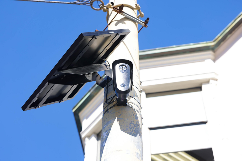 A woman in an orange shirt holds hands with a child wearing a brown hat as they sit on a metal bench facing a city skyline.